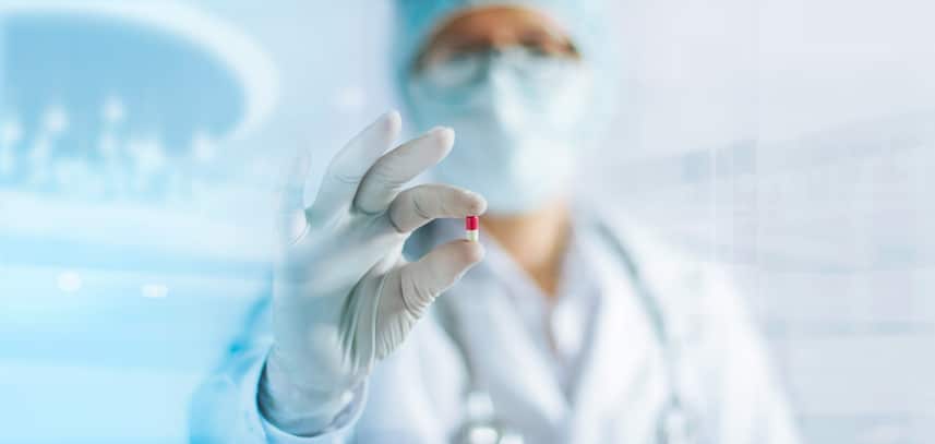 Medicine doctor holding a color capsule pill in hand with white glove in laboratory background